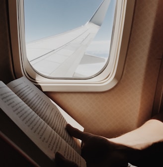 person reading book beside airplane window