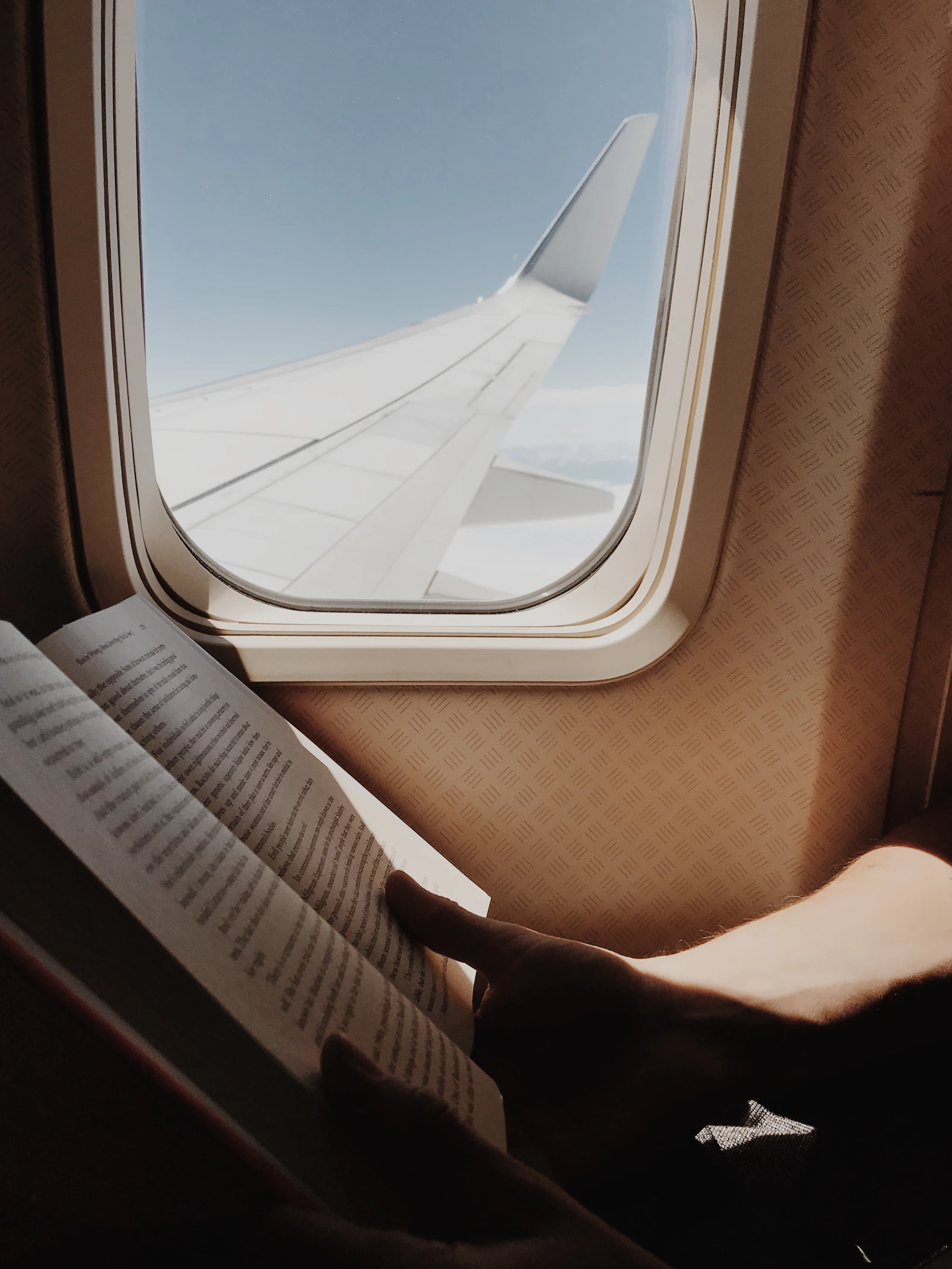 A traveller reads beside an aircraft window with daylight beyond the glass.