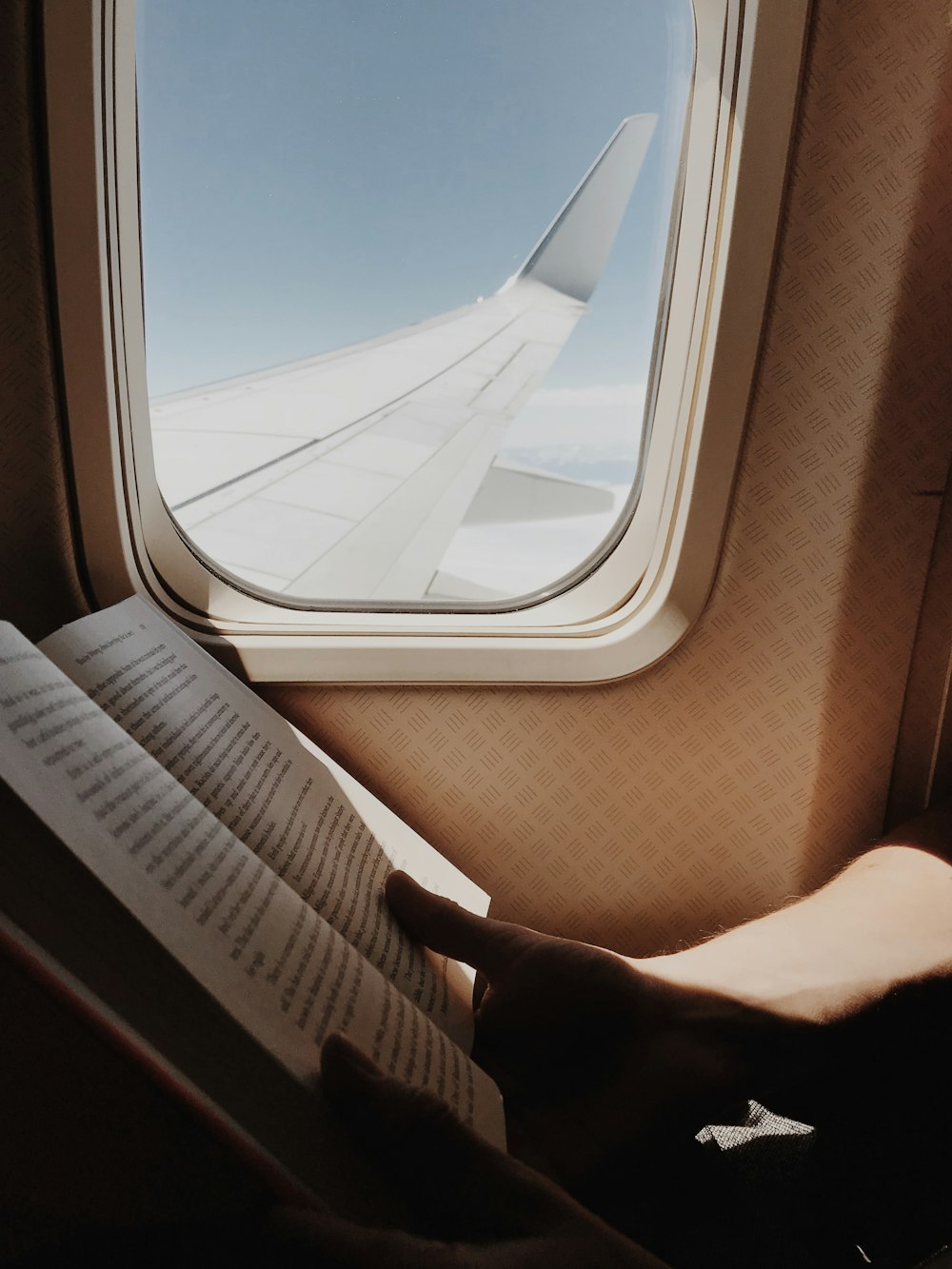 person reading book beside airplane window