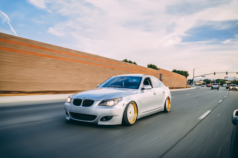 silver BMW sedan passing by near brown wall