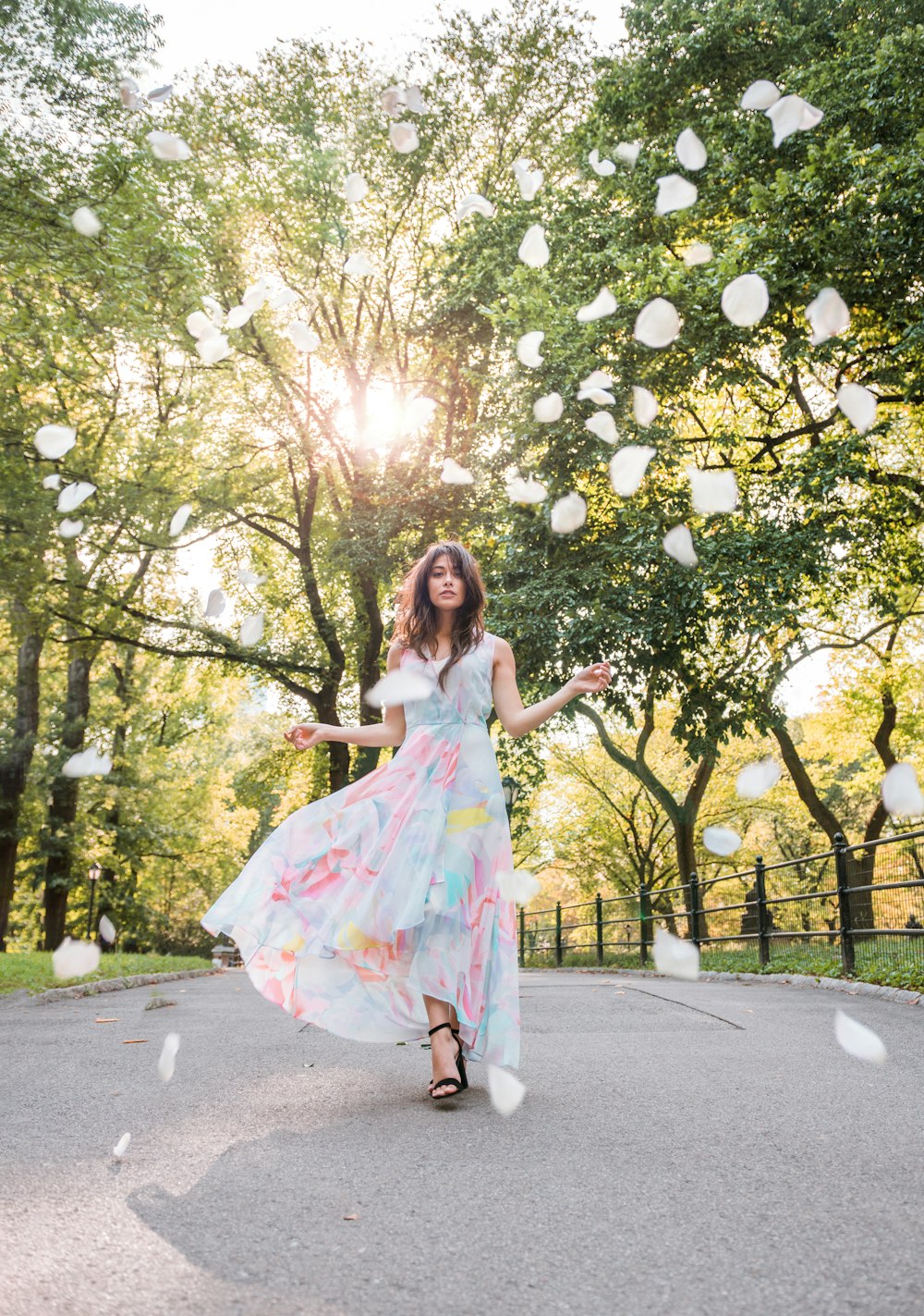 woman in floral maxi dress walking on street between trees