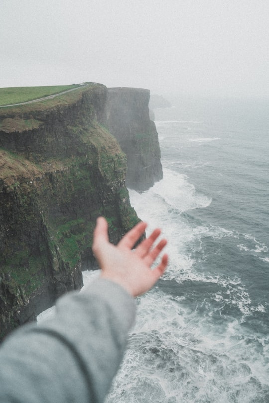 person standing on the cliff near the ocean in Cliffs of Moher Ireland