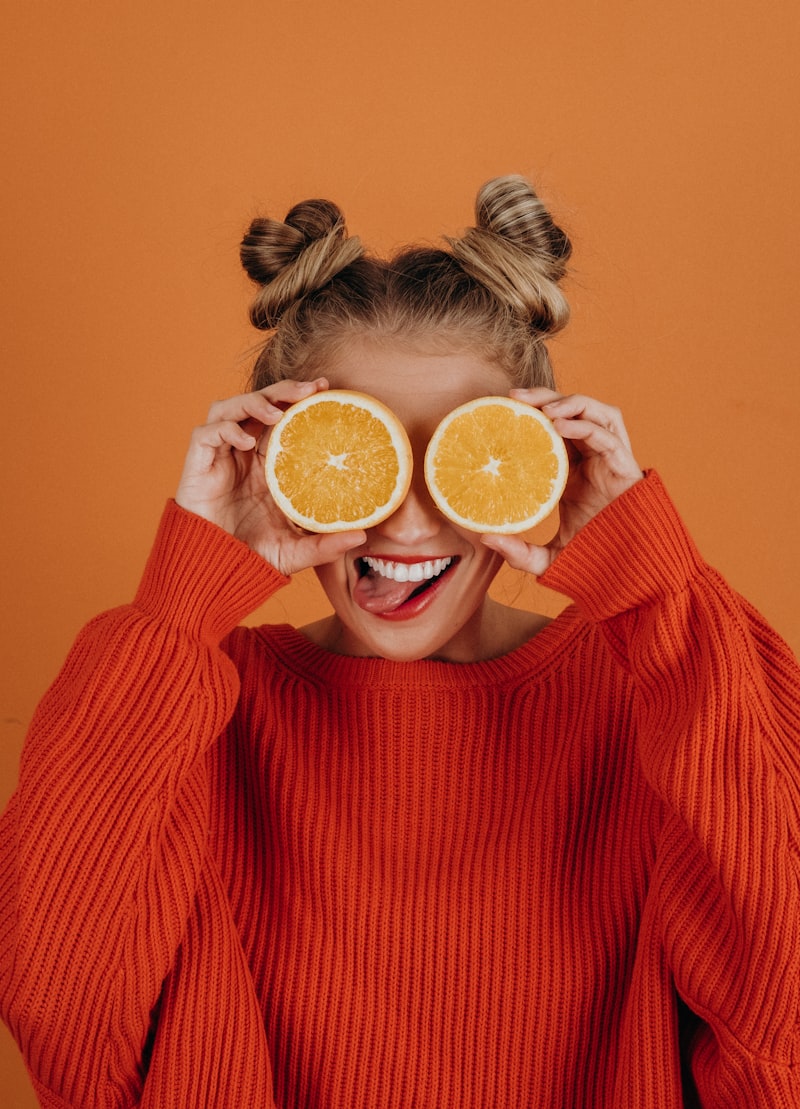 Woman in Orange Blouse holding orange slices over her eyes