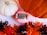 A pink colored bath bomb labeled 'Antidote Stress/Anxiety Bath Bomb' with a 'Pumpkin Spice' tag is placed between a white and an orange pumpkin. Surrounding these items is decorative shredded paper in black and orange colors, creating a festive atmosphere.