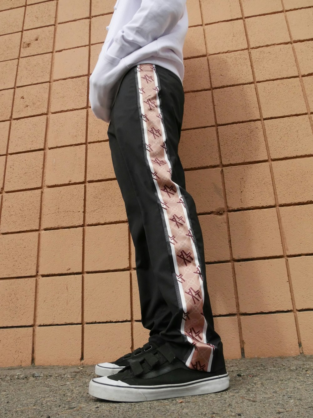 person wearing white hoodie, black and brown pants, and pair of black-and-white shoes