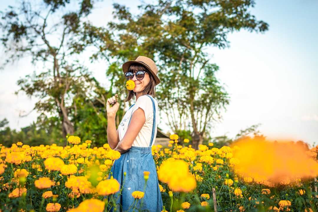 woman in blue denim overalls holding yellow flower