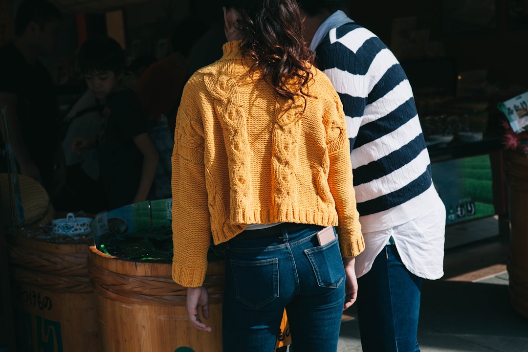 woman in yellow knit sweater and blue denim jeans stands beside man