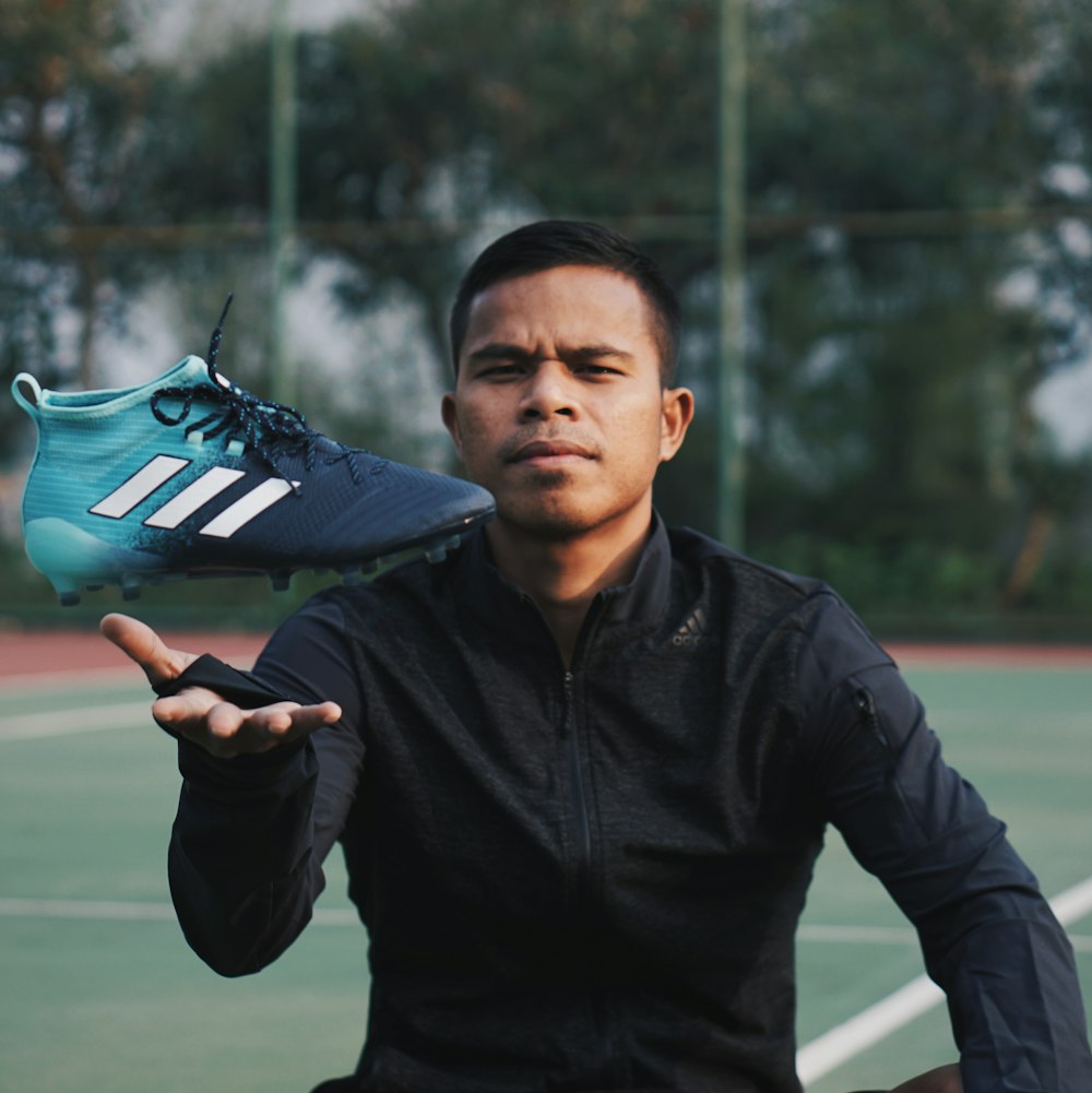 man in black zip-up jacket holding unpaired blue and black adidas cleat  photo – Free Indonesia Image on Unsplash