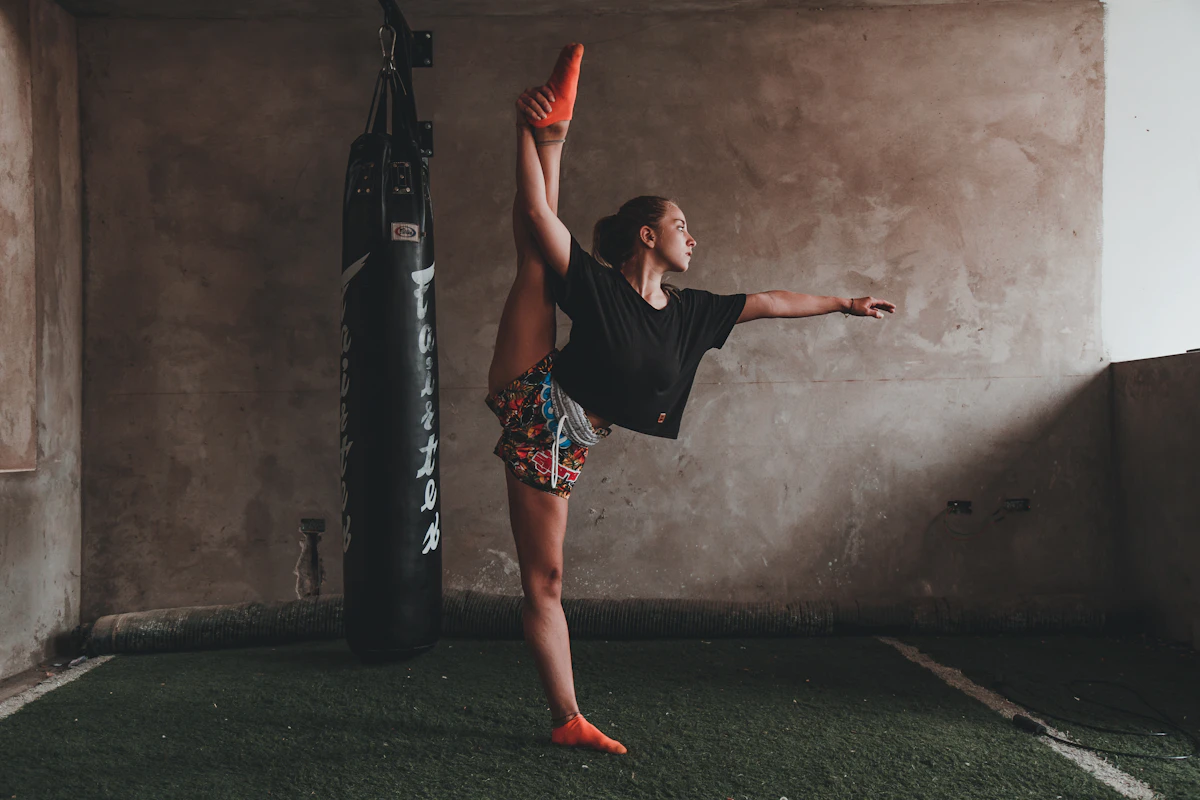 An athlete holding a standing split beside a heavy bag