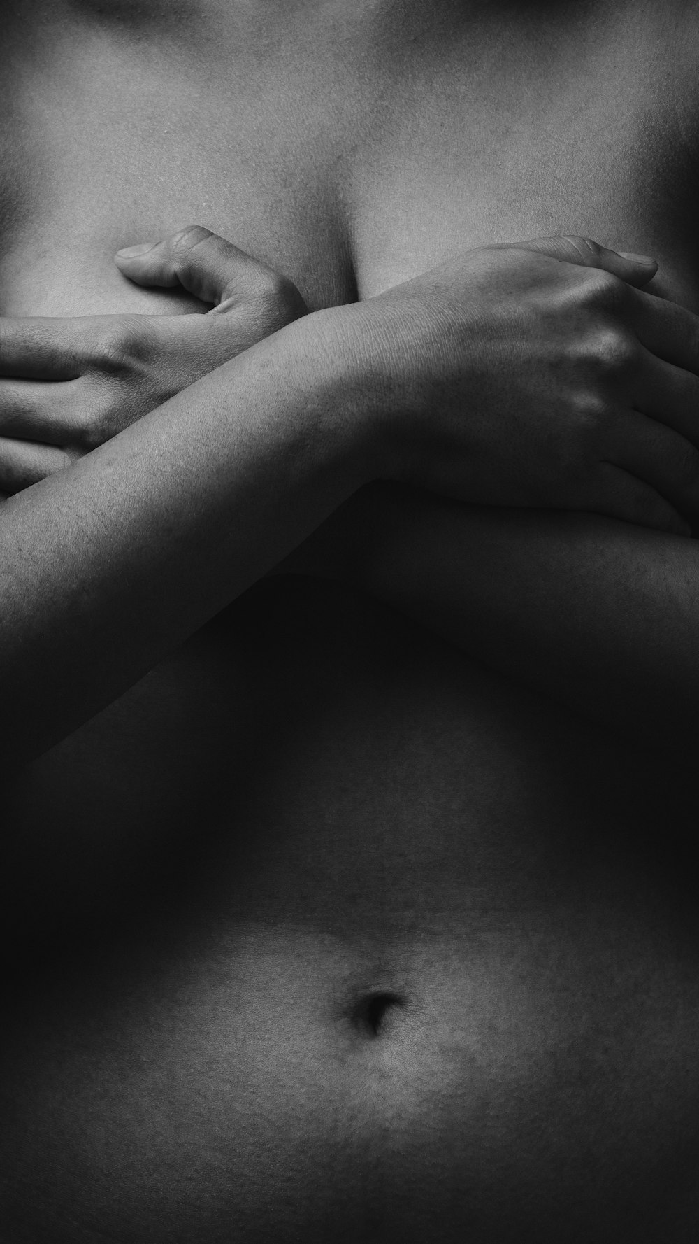 Foto en escala de grises de una mujer cubriendo su pecho con ambas manos