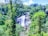 A cascading waterfall surrounded by lush tropical forest with vibrant green foliage and tall trees. The water flows over rocky terrain, creating a serene and natural landscape.
