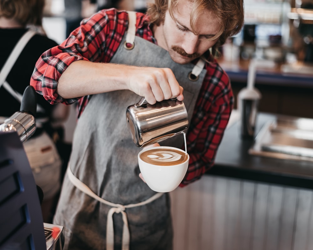 hombre vertiendo leche en una taza de capuchino