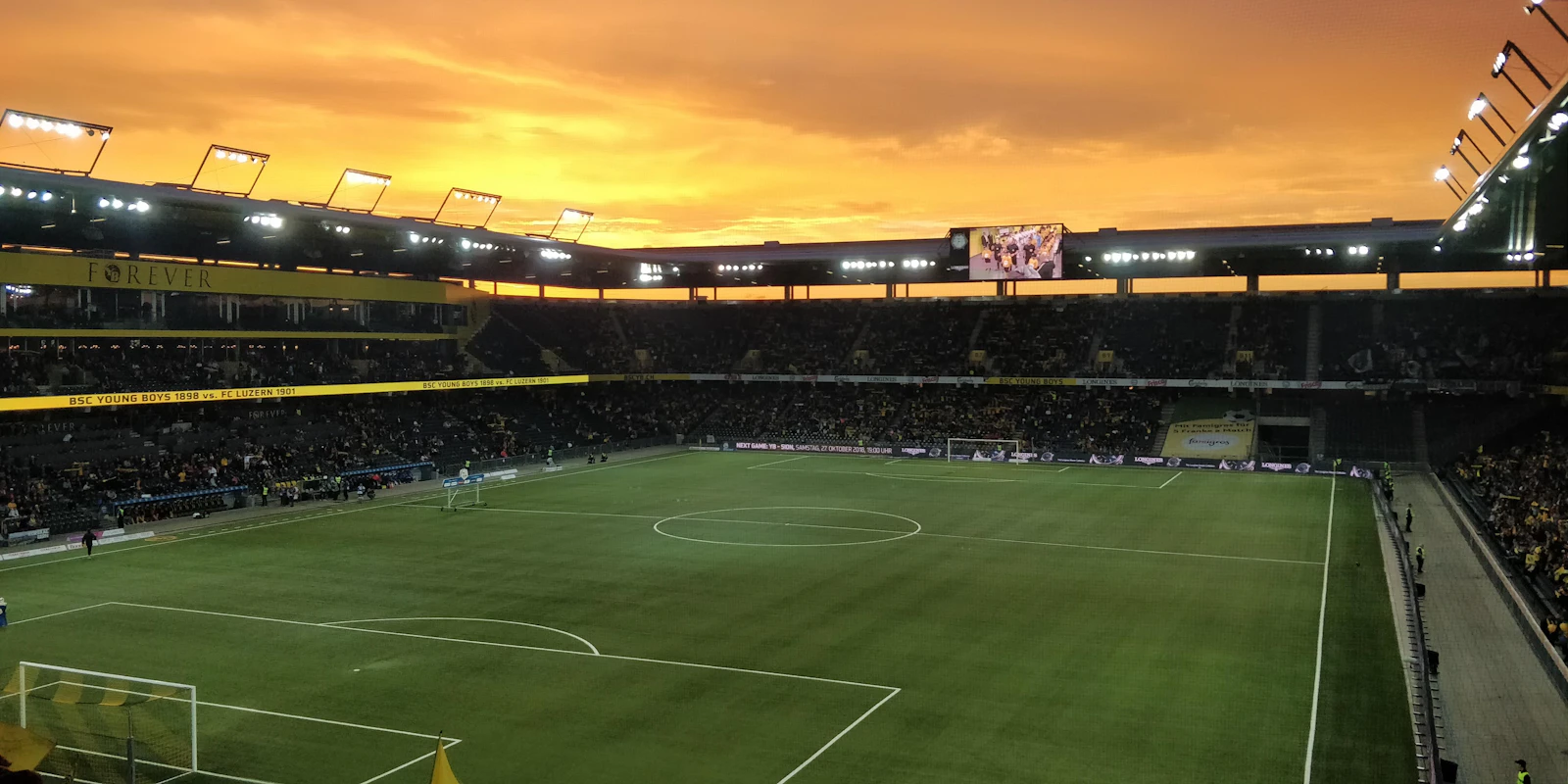 An empty football pitch inside a stadium under an orange sunset sky