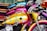 A row of vibrantly colored motorcycles lined up next to each other. The foremost motorcycle features a golden-yellow tank adorned with blue stars and shiny chrome details. Behind it, other bikes display shades of pink and blue with similar chrome accents. The seats are made of rich, brown leather.