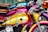 A row of vibrantly colored motorcycles lined up next to each other. The foremost motorcycle features a golden-yellow tank adorned with blue stars and shiny chrome details. Behind it, other bikes display shades of pink and blue with similar chrome accents. The seats are made of rich, brown leather.
