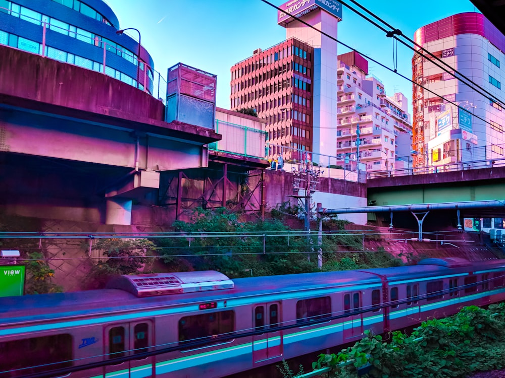 a train traveling past tall buildings under a bridge