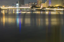 Nighttime cityscape with glowing lights reflecting off a calm river.