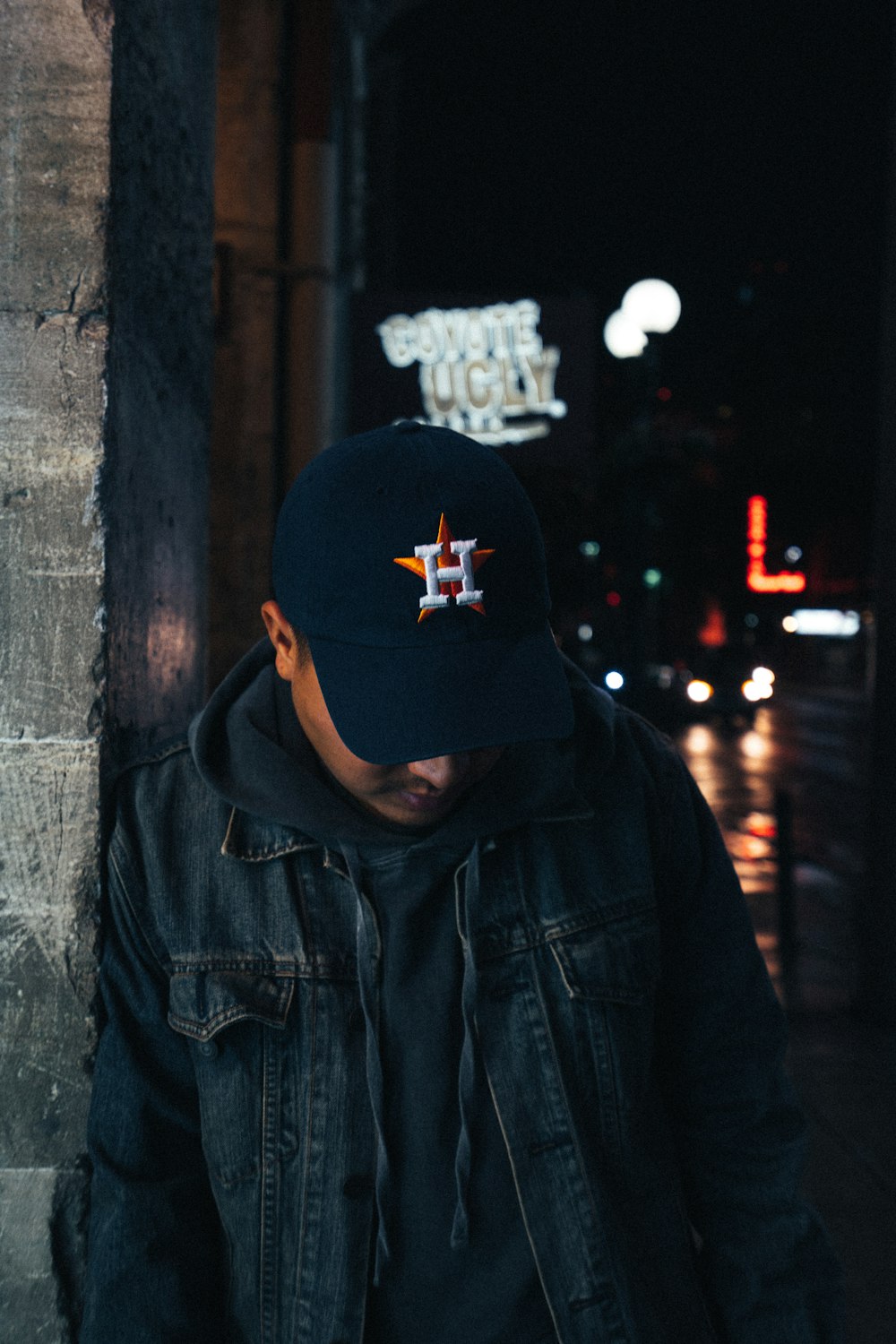 man wearing black denim jacket leaning on wall