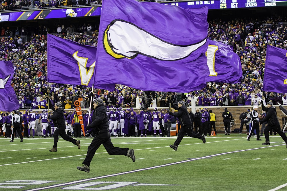 people running and holding Minnesota Vikings flags in green field