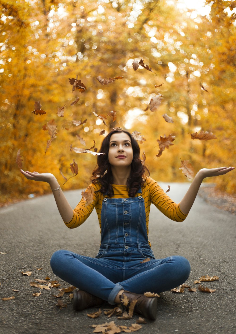 personne assise avec les jambes croisées jetant des feuilles en l’air