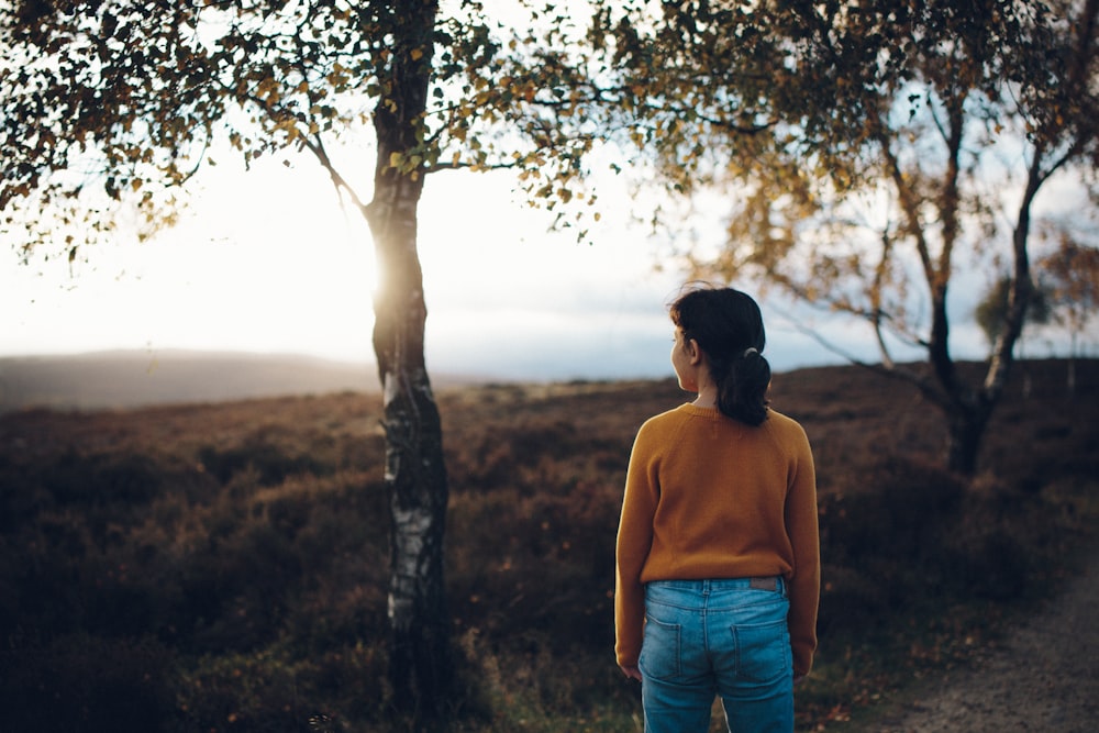 woman wearing brown sweater standing beside tree during daytime