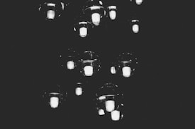 A series of glowing light bulbs suspended in mid-air against a dark background, creating a floating effect. The lights appear to be enclosed within clear glass spheres, emitting a soft, ethereal glow.