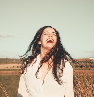 A joyful woman running her fingers through voluminous, healthy hair outdoors.