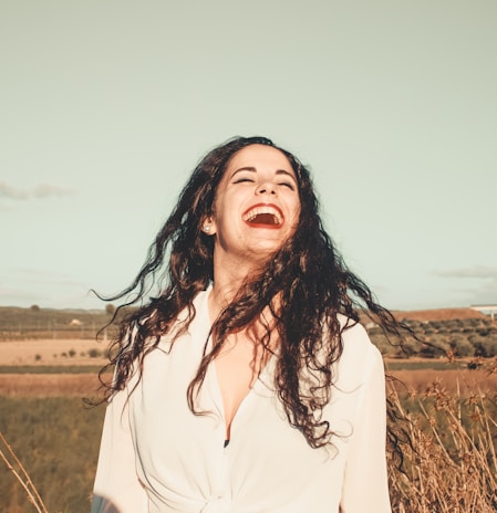 A joyful woman running her fingers through voluminous, healthy hair outdoors.