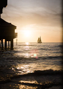 Wide-angle view of a sailboat cutting through calm waters under a warm, glowing sunset sky.