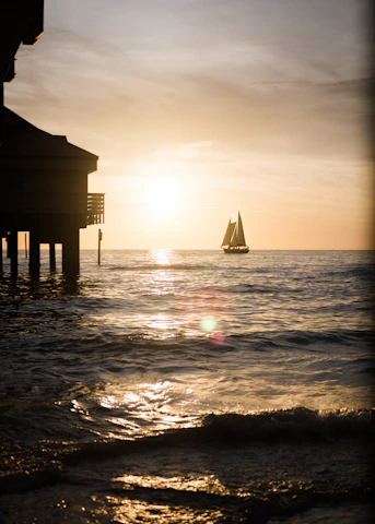 Wide-angle view of a sailboat cutting through calm waters under a warm, glowing sunset sky.