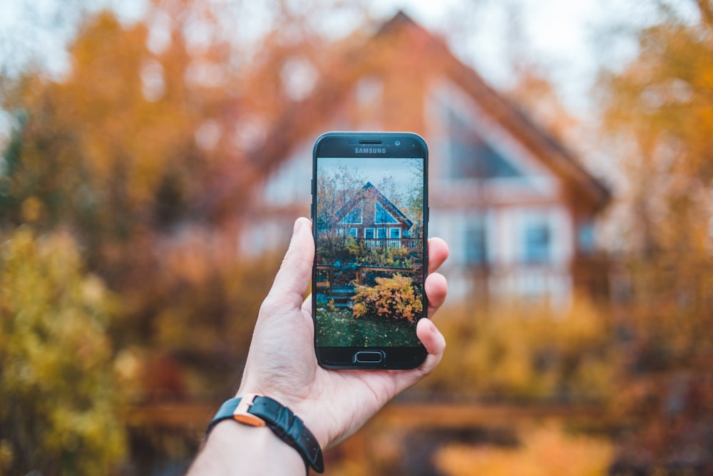 pessoa segurando smartphone Samsung preto tirando uma foto da casa