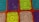 A detailed crochet pattern composed of colorful squares. Each square is crafted with intricate designs, featuring spirals and loops. The colors include bright turquoise, purple, vibrant green, and beige, all framed by a bold orange border.