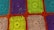 A detailed crochet pattern composed of colorful squares. Each square is crafted with intricate designs, featuring spirals and loops. The colors include bright turquoise, purple, vibrant green, and beige, all framed by a bold orange border.