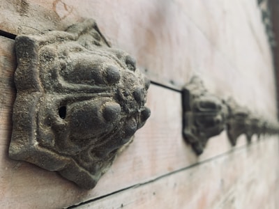 A series of ornately carved metal details are mounted along the surface of a weathered wooden surface. These round, decorative features have an aged, patinated look, suggesting they have withstood time and elements.