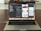 A MacBook Pro is displayed on a wooden table with the screen showing an open code editor. The editor has several lines of code, possibly in Swift, and multiple panes visible, including a project navigator on the left and a simulated iPhone screen in the center displaying a news app. The laptop's dock is visible with several application icons. The background is blurred, focusing attention on the laptop.