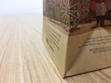 A close-up view of a paper bag on a wooden surface, depicting an illustration with a wagon wheel and people. The bag has printed text describing its contents and ingredients.