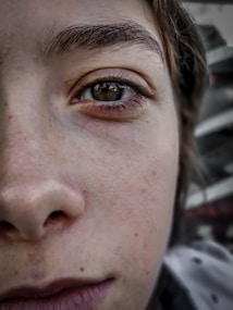 A close-up view of a person's face, focusing on the eye and surrounding skin. The image showcases detailed textures of the skin and the eye's reflection. The background is blurred, drawing attention to the subject.
