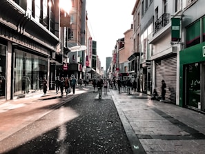 A bustling downtown street filled with people and colorful storefronts on a sunny day.