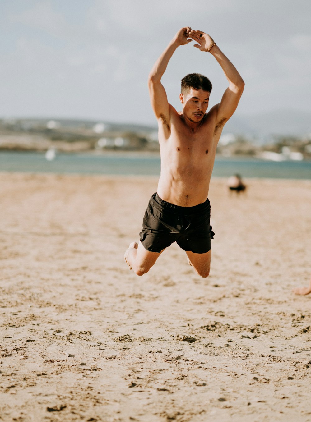 uomo che indossa pantaloncini neri che salta in riva al mare