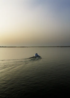 Wide-angle view of a lone boat cutting through gentle waves under a bright terracotta-hued sky.