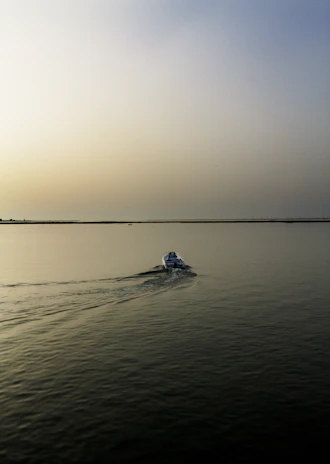 Wide-angle view of a lone boat cutting through gentle waves under a bright terracotta-hued sky.