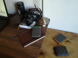 Stacks of international shipping documents and a laptop on a wooden desk.