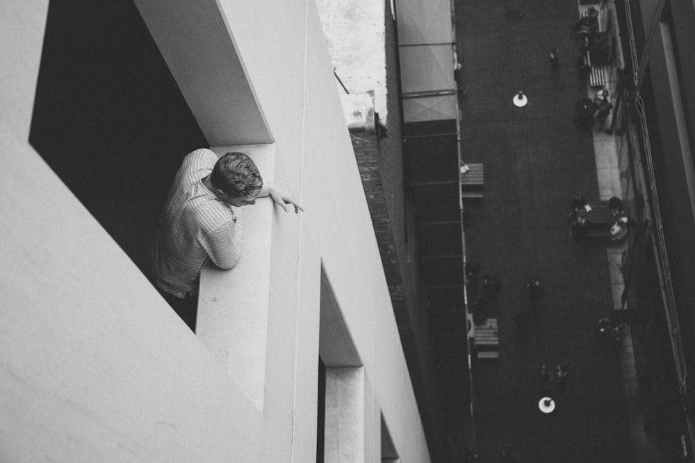 grayscale photo of man beside window