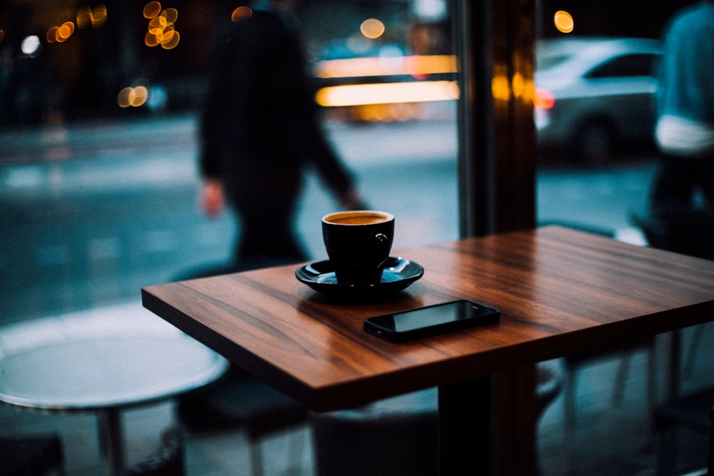 taza de café y teléfono inteligente encima de la mesa de comedor de madera