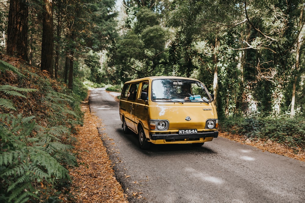 緑の木々の下の道路を走る茶色のバン