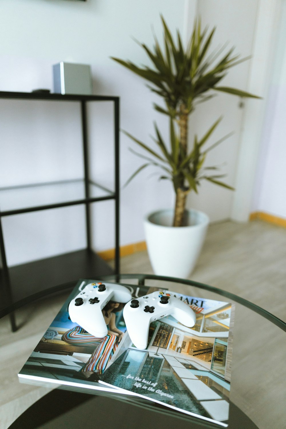 two Xbox One game controllers on magazine book on top of glass table