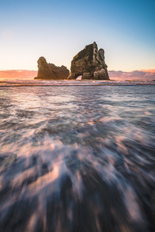 rock formation on body of water during daytime in Wharariki Beach New Zealand