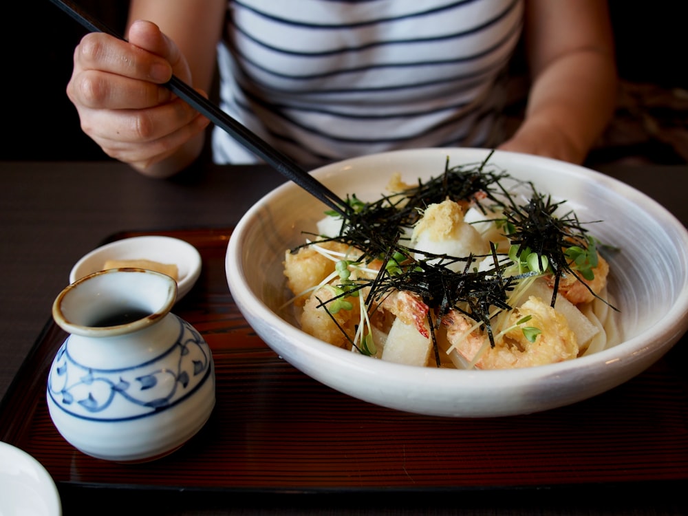 woman holding chopsticks with cooked food in bowl on table