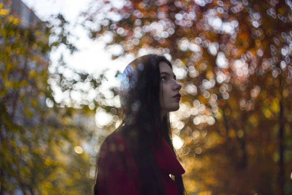 selective focus photo of woman standing under green trees