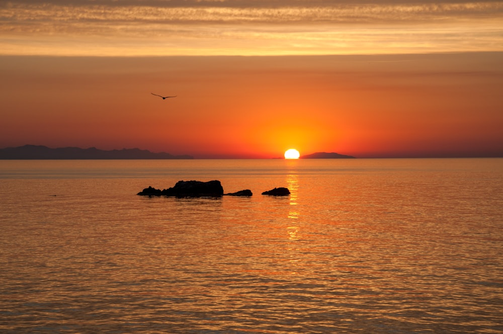 silhouette of rock formation on sea during sunset